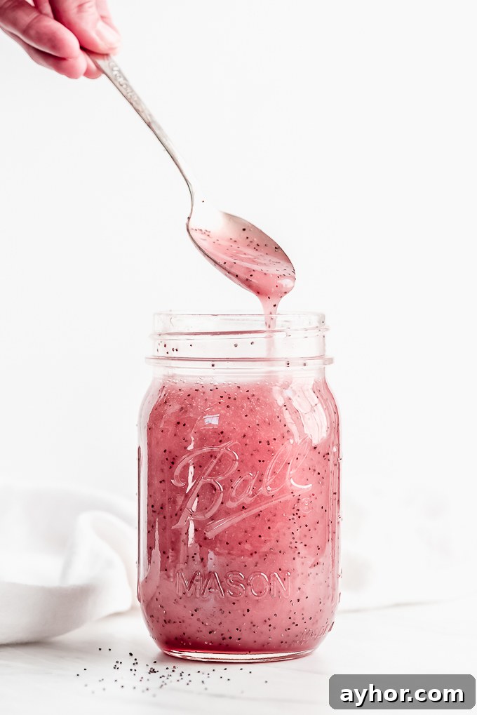 A large jar of pink poppy seed dressing with a spoon lifting some out and letting it stream back into the jar.