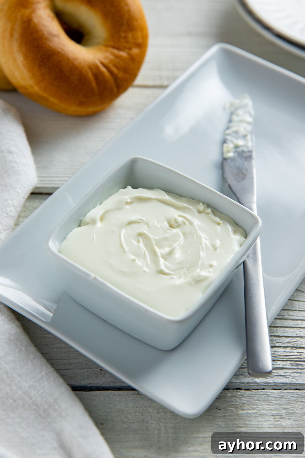 Cream Cheese Substitutes: 30+ Swaps for Any Recipe 2 Cream cheese in a square white bowl on a rectangular white platter with a knife on the side. A bagel in the background.