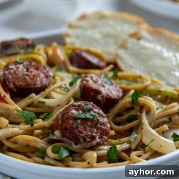 Cooked Cajun spaghetti on white plate with two slices of buttered French bread on the side.