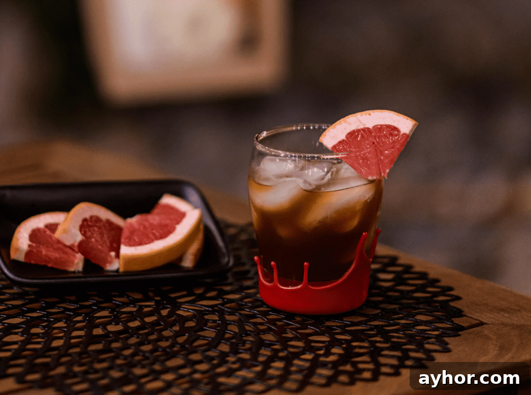 20+ Spooky Halloween Cocktail Recipes for Adults 15 Dark cocktail on table with grapefruit slice.