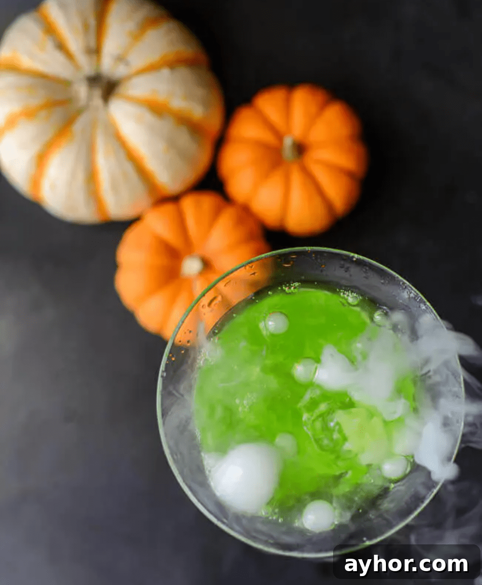 20+ Spooky Halloween Cocktail Recipes for Adults 9 Bubbly green drink on table with pumpkins.