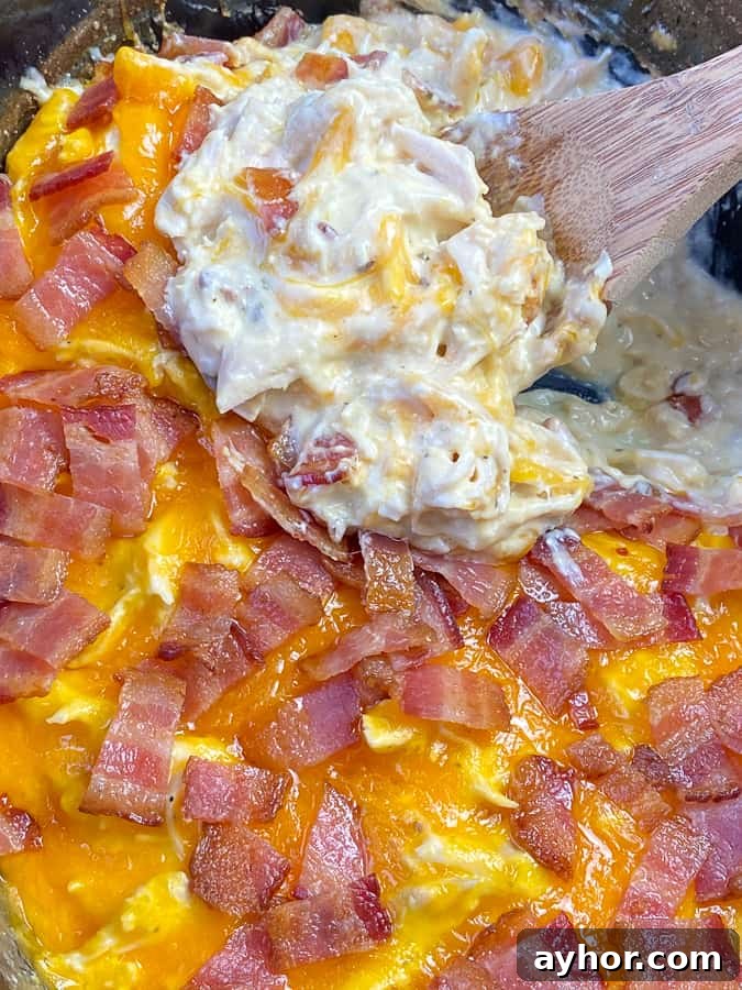 Slow Cooker Chicken with Bacon and Ranch Flavor 2 Close up of slow cooker shredded chicken covered in cheese and bacon with a wooden spoon lifting a serving out of the crock.