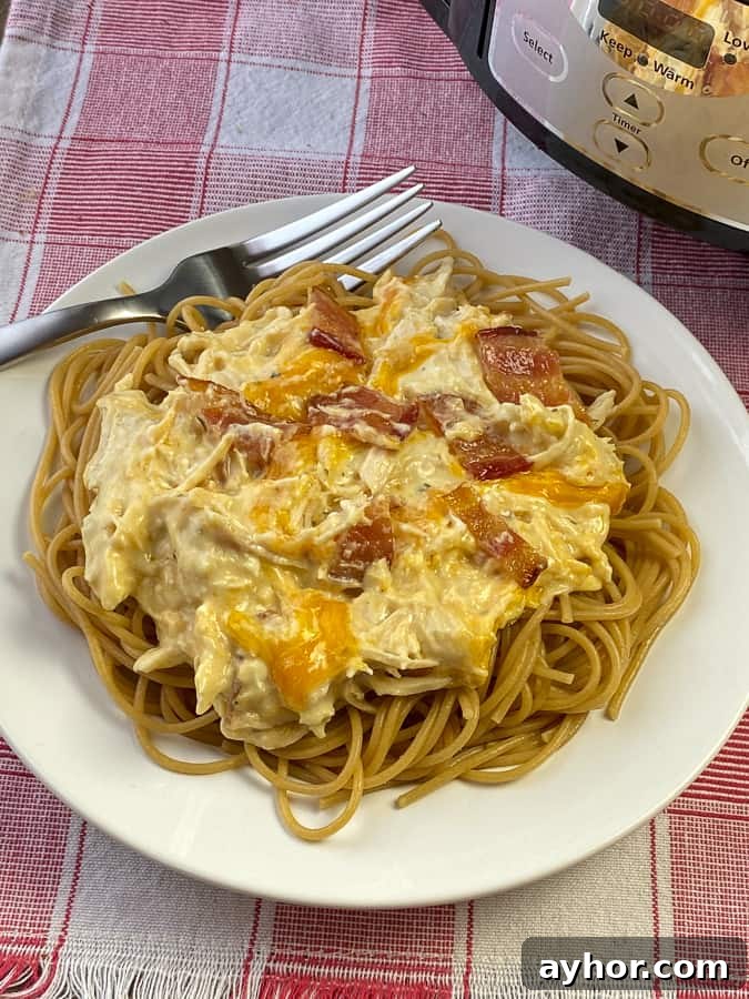 Slow Cooker Chicken with Bacon and Ranch Flavor 5 Crack chicken over spaghetti pasta on white plate with fork.
