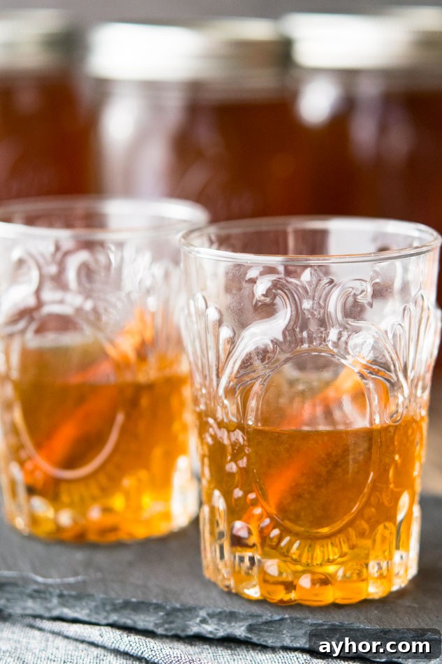 Spice up the holidays with apple pie moonshine, the fiery beverage of outlaws domesticated by a touch of grandma’s apple pie. A unique gift for adult pals. #moonshine #applepiemoonshine Two glasses of Apple Pie Moonshine with cinnamon sticks