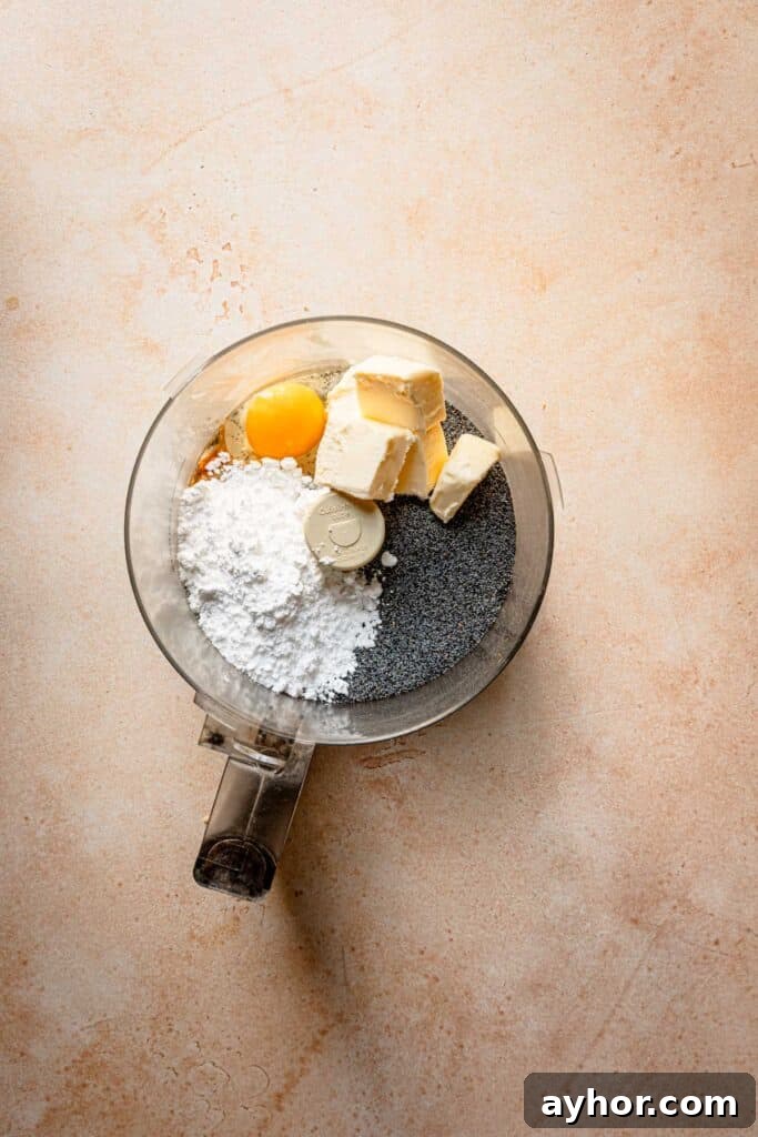 A food processor bowl with poppy seeds, butter, egg and powdered sugar.