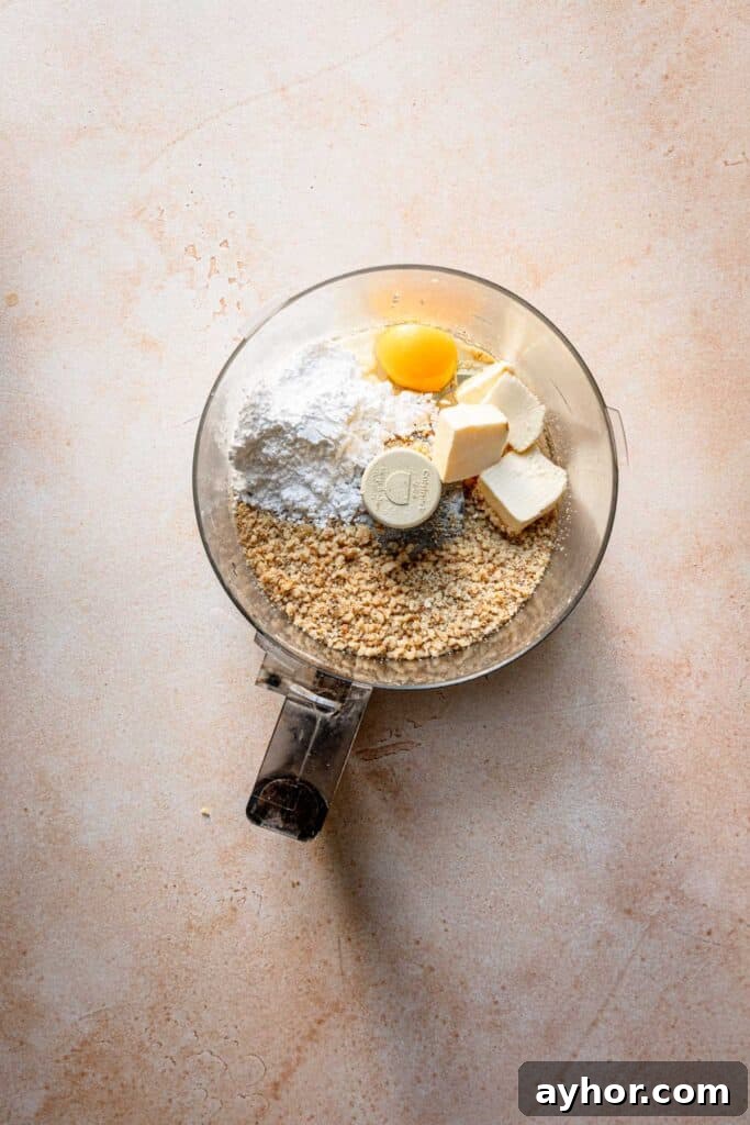 A food processor bowl with ground walnuts, butter, egg and powdered sugar.