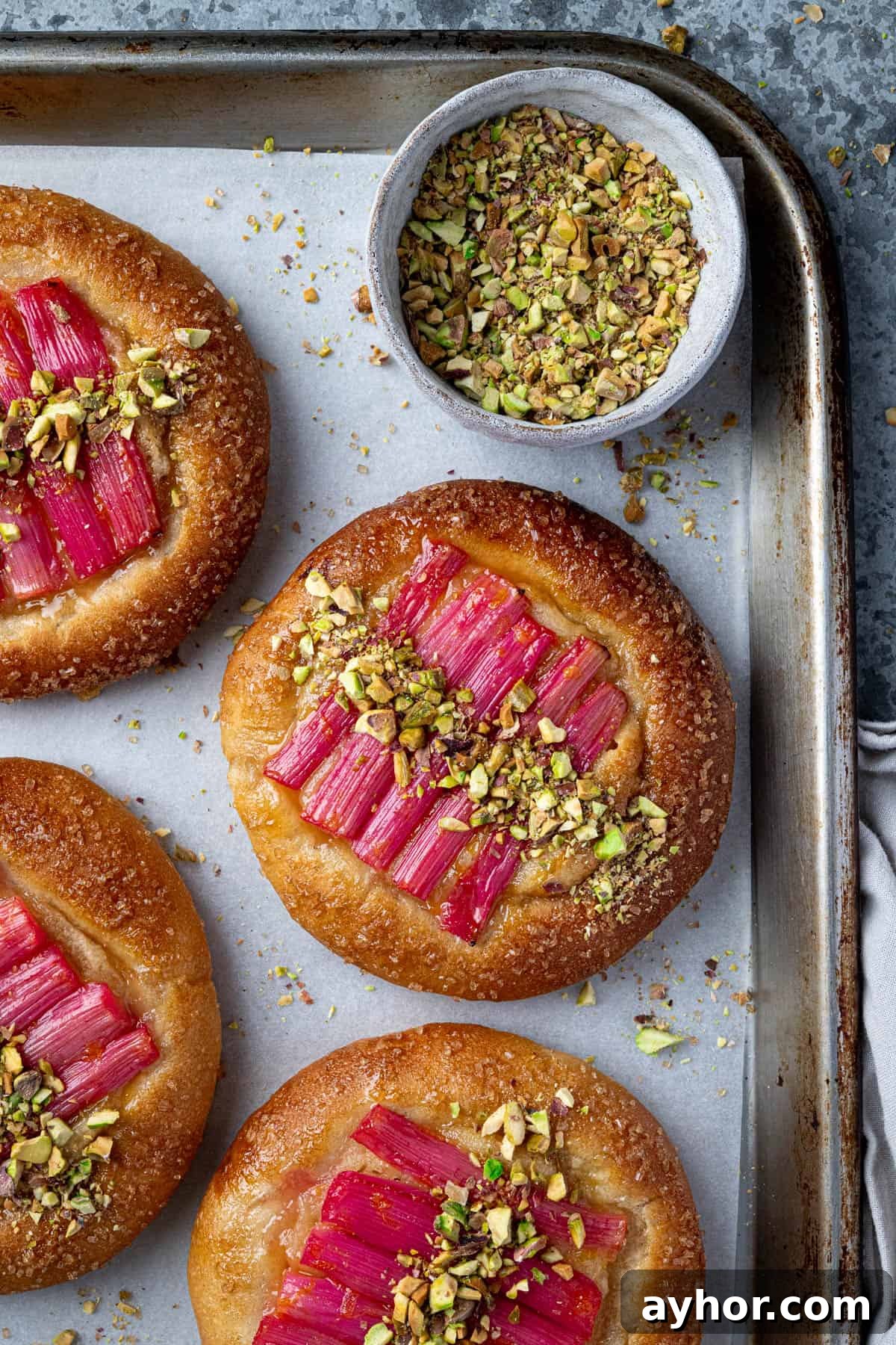 Vegan Rhubarb Frangipane Buns Recipe: Flaky Pastries with Almond Filling 2 Rhubarb frangipane buns on a baking tray with a bowl of chopped pistachios.