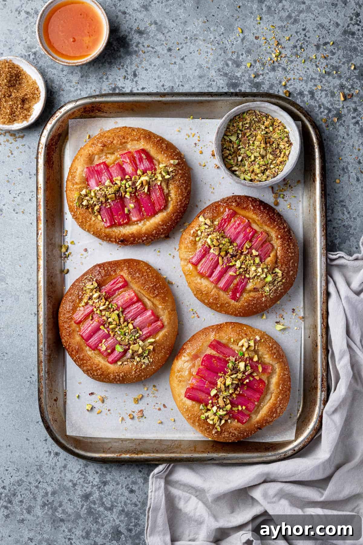 Vegan Rhubarb Frangipane Buns Recipe: Flaky Pastries with Almond Filling 15 Rhubarb frangipane buns on a baking sheet with a bowl of chopped pistachios.
