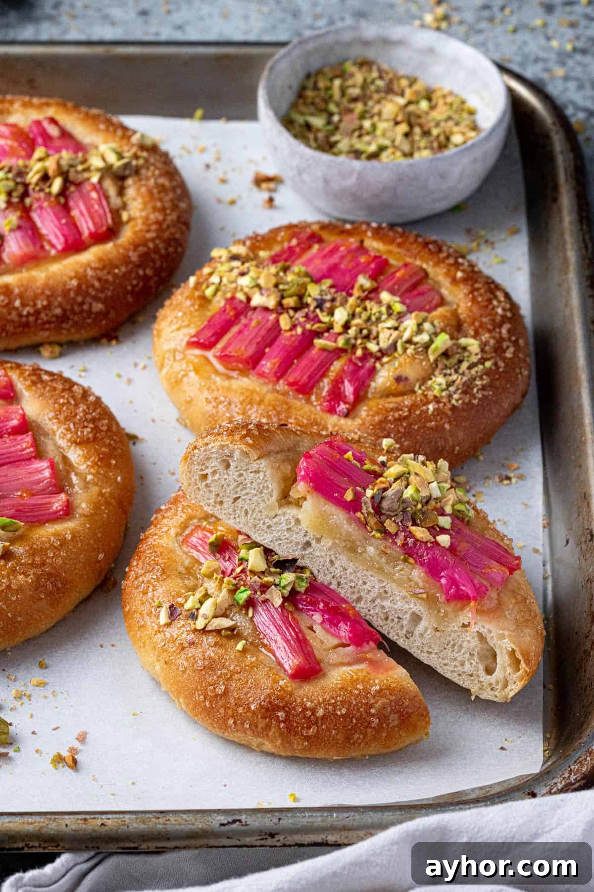 Vegan Rhubarb Frangipane Buns Recipe: Flaky Pastries with Almond Filling 17 Rhubarb frangipane buns on a baking sheet, one of them sliced in half.