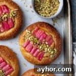 Vegan Rhubarb Frangipane Buns Recipe: Flaky Pastries with Almond Filling 18 Rhubarb frangipane buns on a baking tray with a bowl of chopped pistachios.