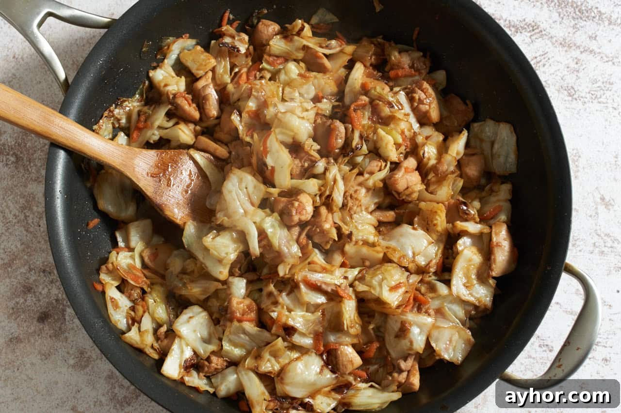Finished chicken and cabbage stir fry in a skillet with a bamboo spatula.