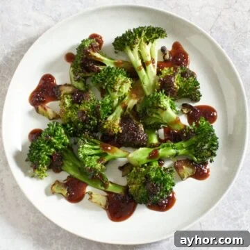 Spicy asian broccoli on a white plate drizzled with a spicy sauce that is reddish-brown in color.