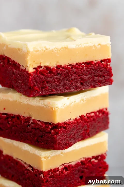 A close up of 4 red velvet millionaire brownies in a stack set against a mottled light background.