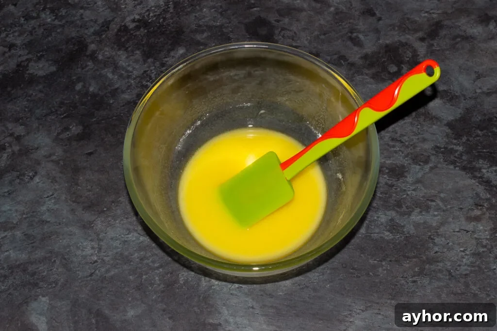Melted butter in a glass mixing bowl with a green spatula