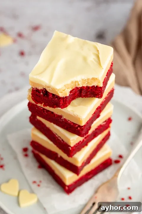 A stack of 5 red velvet millionaire brownies set on two stacked plates with a fork on the side. The top one has a bite taken out of it.