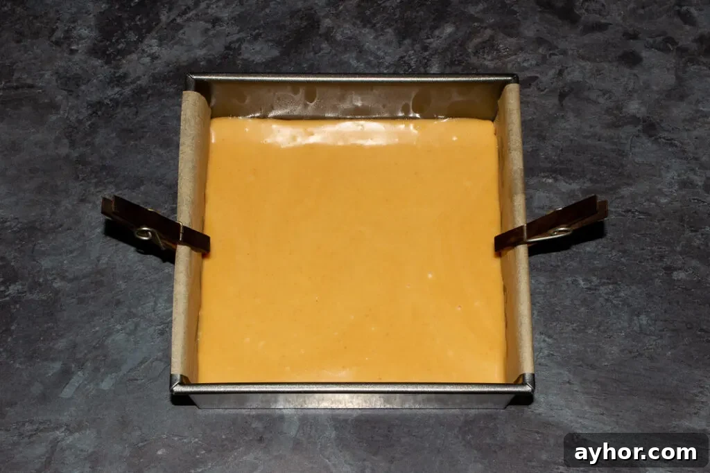 A lined square baking tin with caramel poured over red velvet brownie.