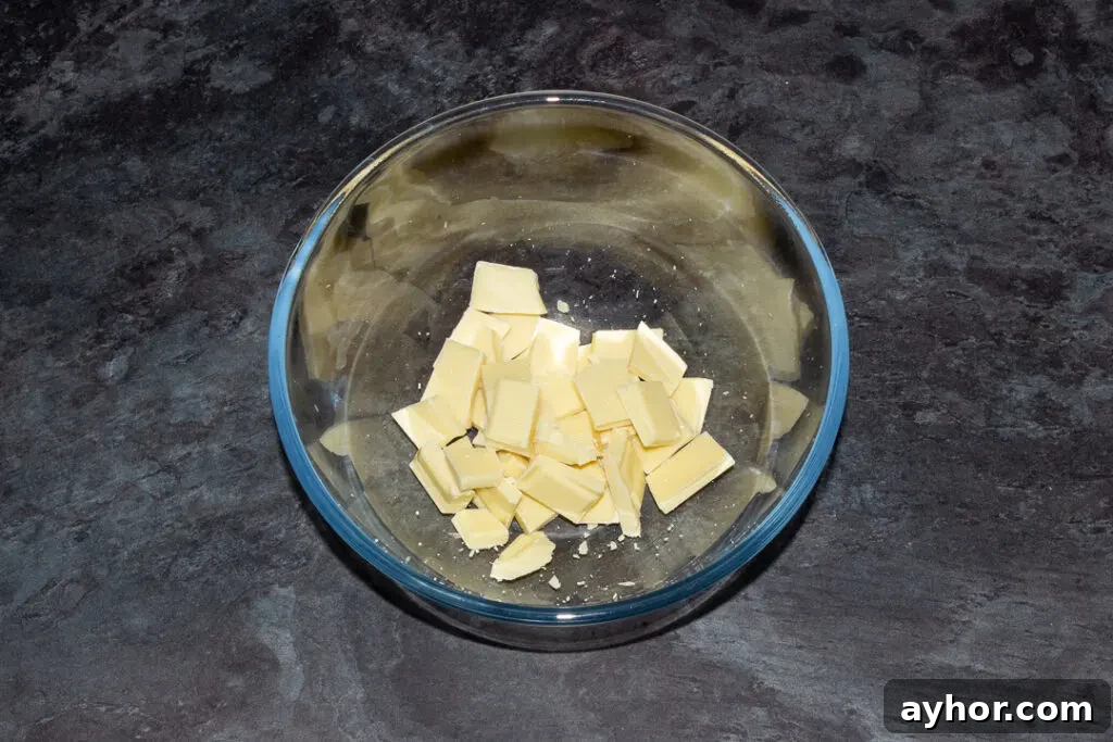 Broken white chocolate in a glass bowl on a kitchen worktop.