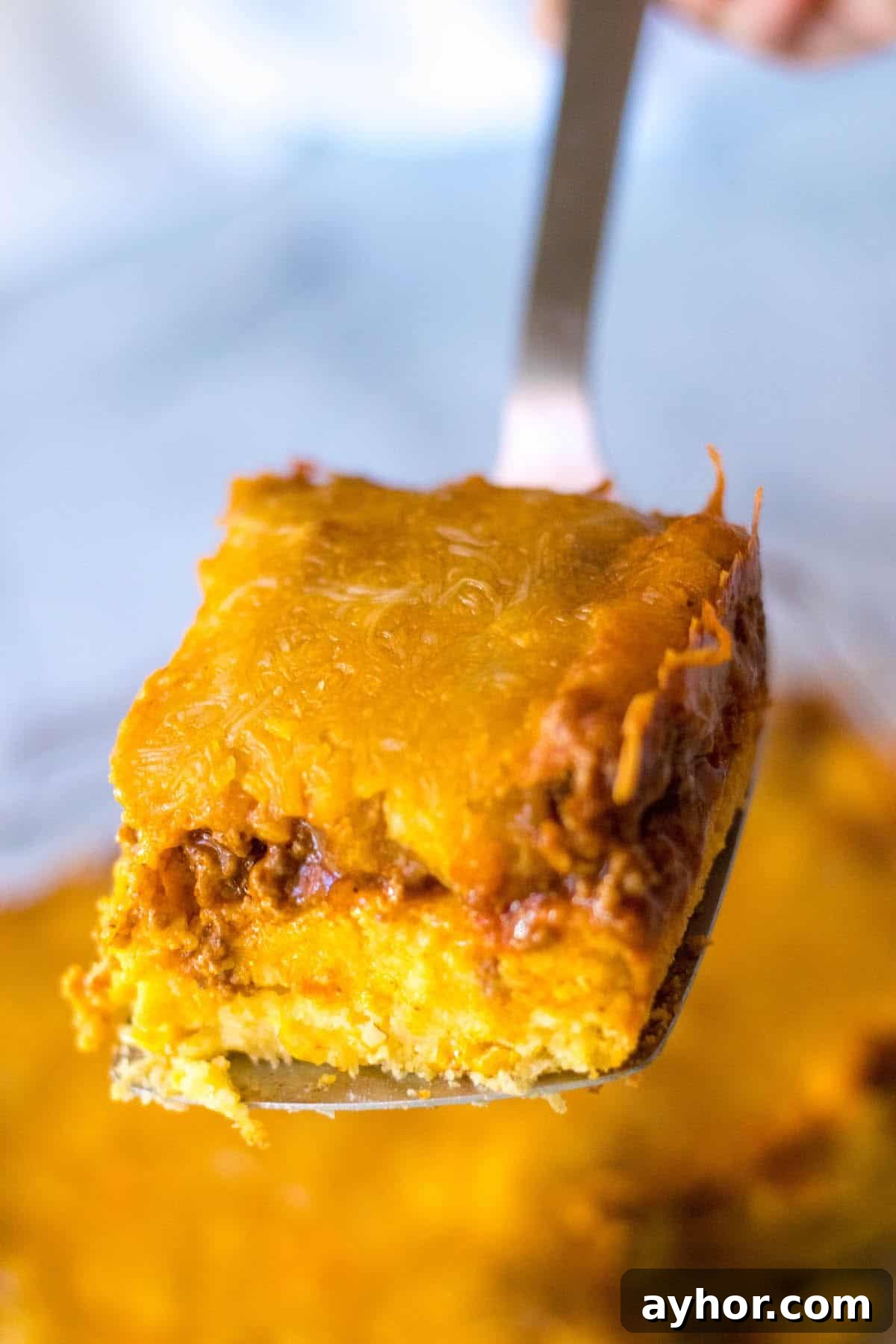 A slice of casserole with cornbread layer, ground beef layer and cheese.