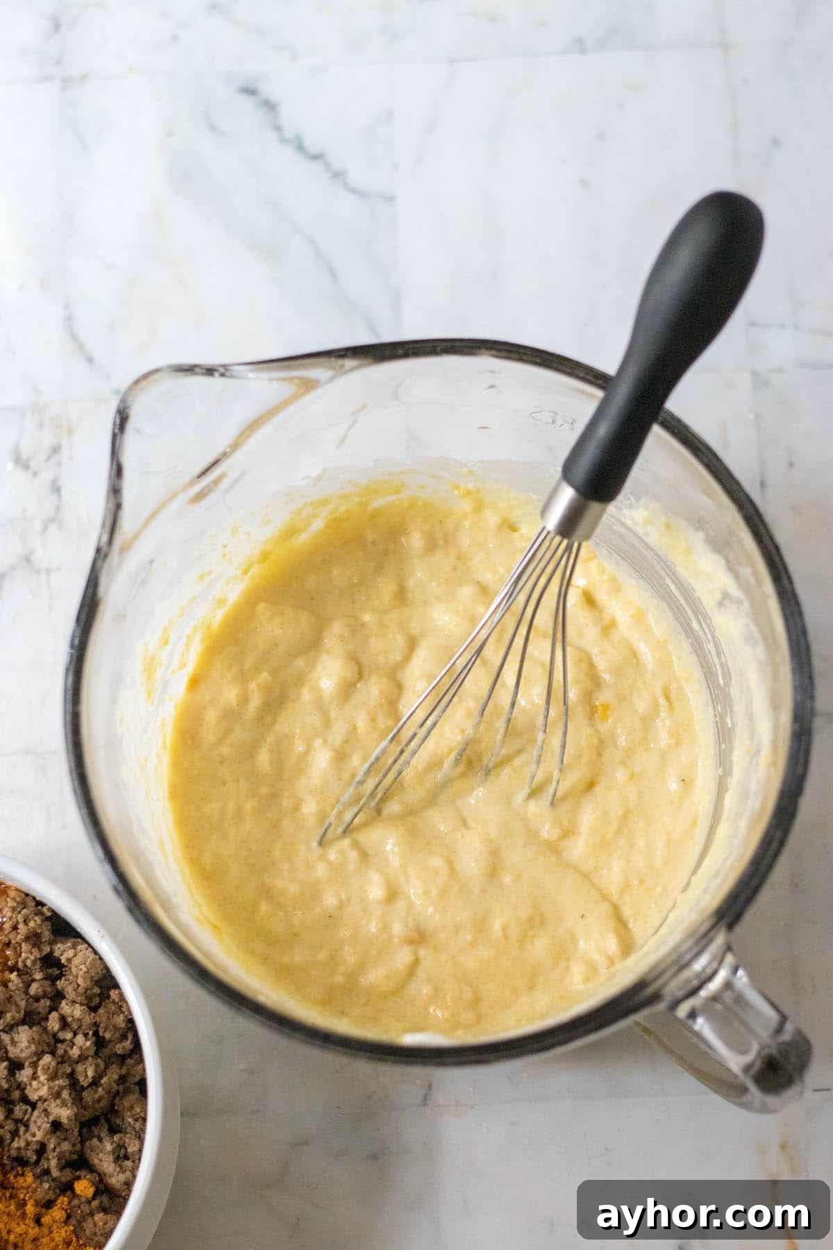 A combined mixture of cornbread mix, creamed corn, sour cream and egg in a mixing bowl.