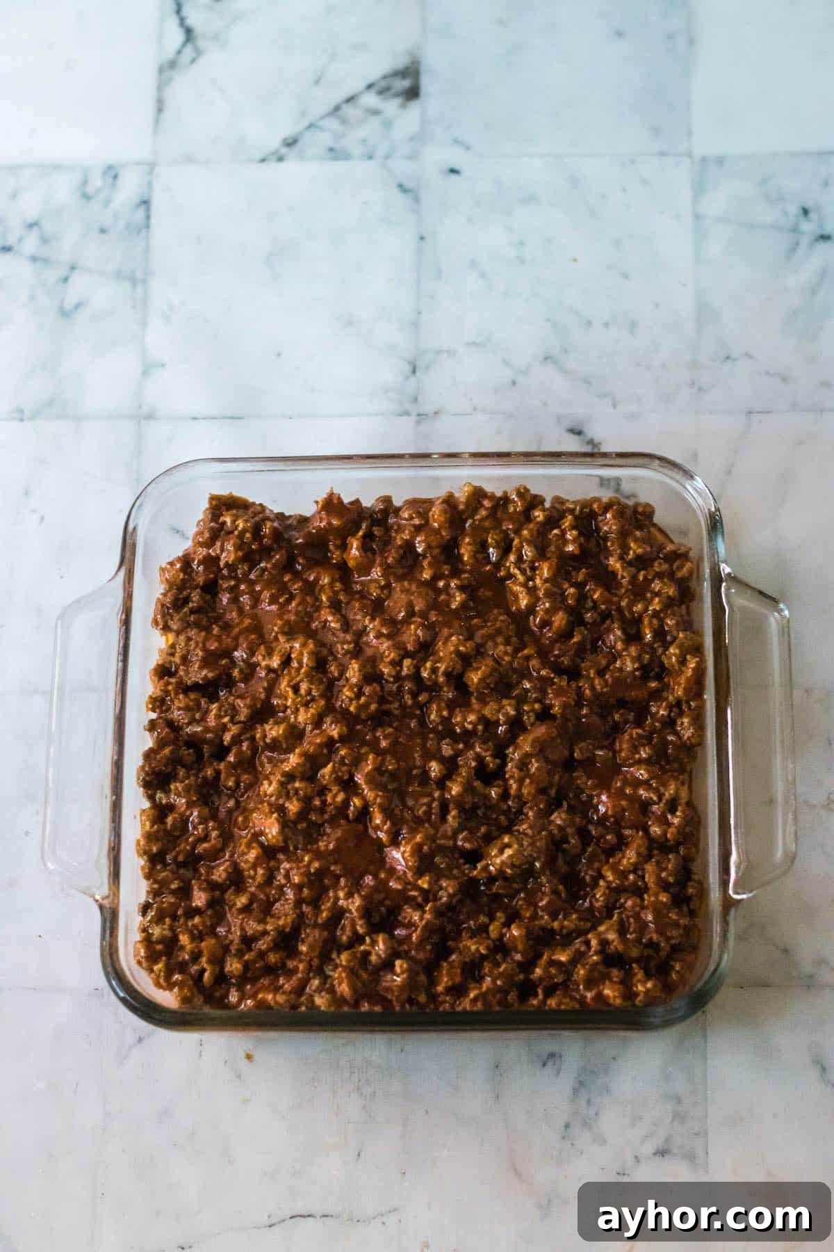 Cornbread mixture topped with a cooked and seasoned ground beef mixture in a square baking dish.