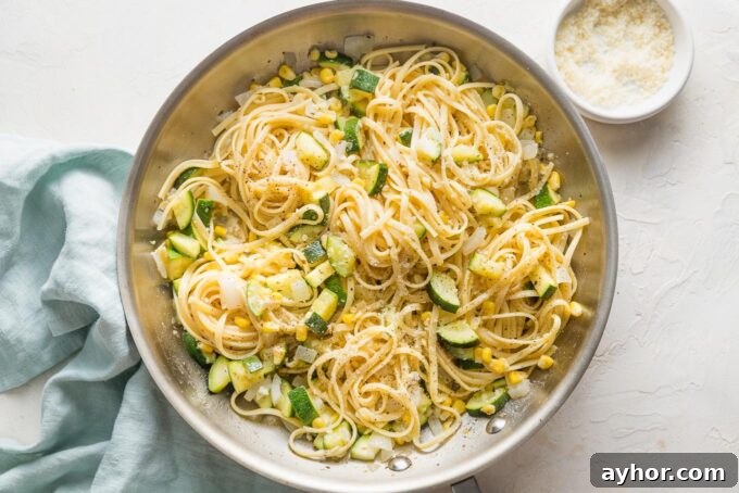 Pasta being added to and tossed with zucchini and corn in a skillet.