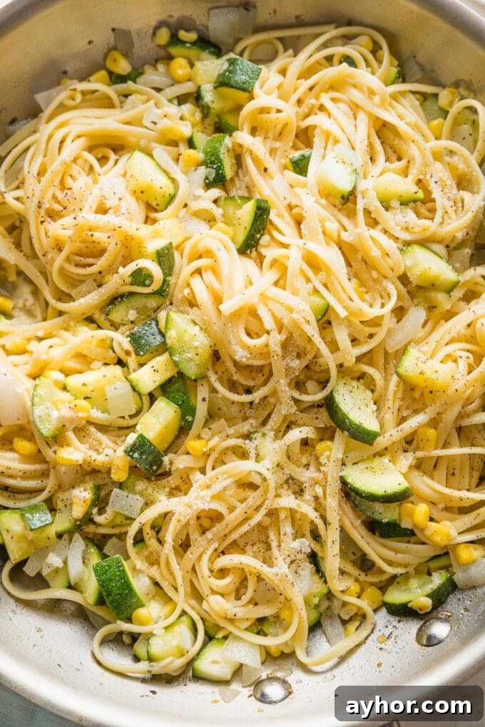 Close up of a skillet holding al dente linguine mixed with zucchini and corn in a light buttery sauce.