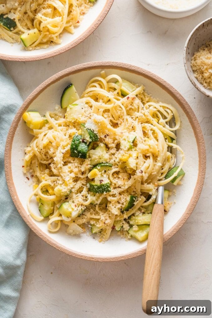 Bowl with a helping of pasta with zucchini and corns in a buttery sauce with toasted breadcrumbs on top.