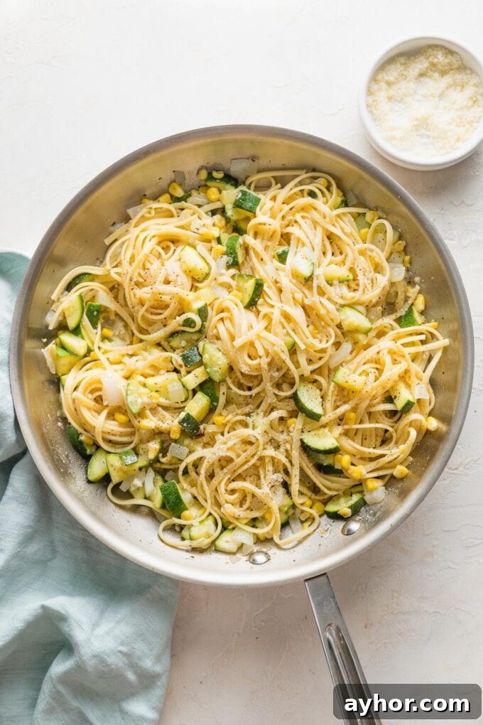 Skillet full of pasta with zucchini and corn in a light white wine butter sauce with Parmesan.