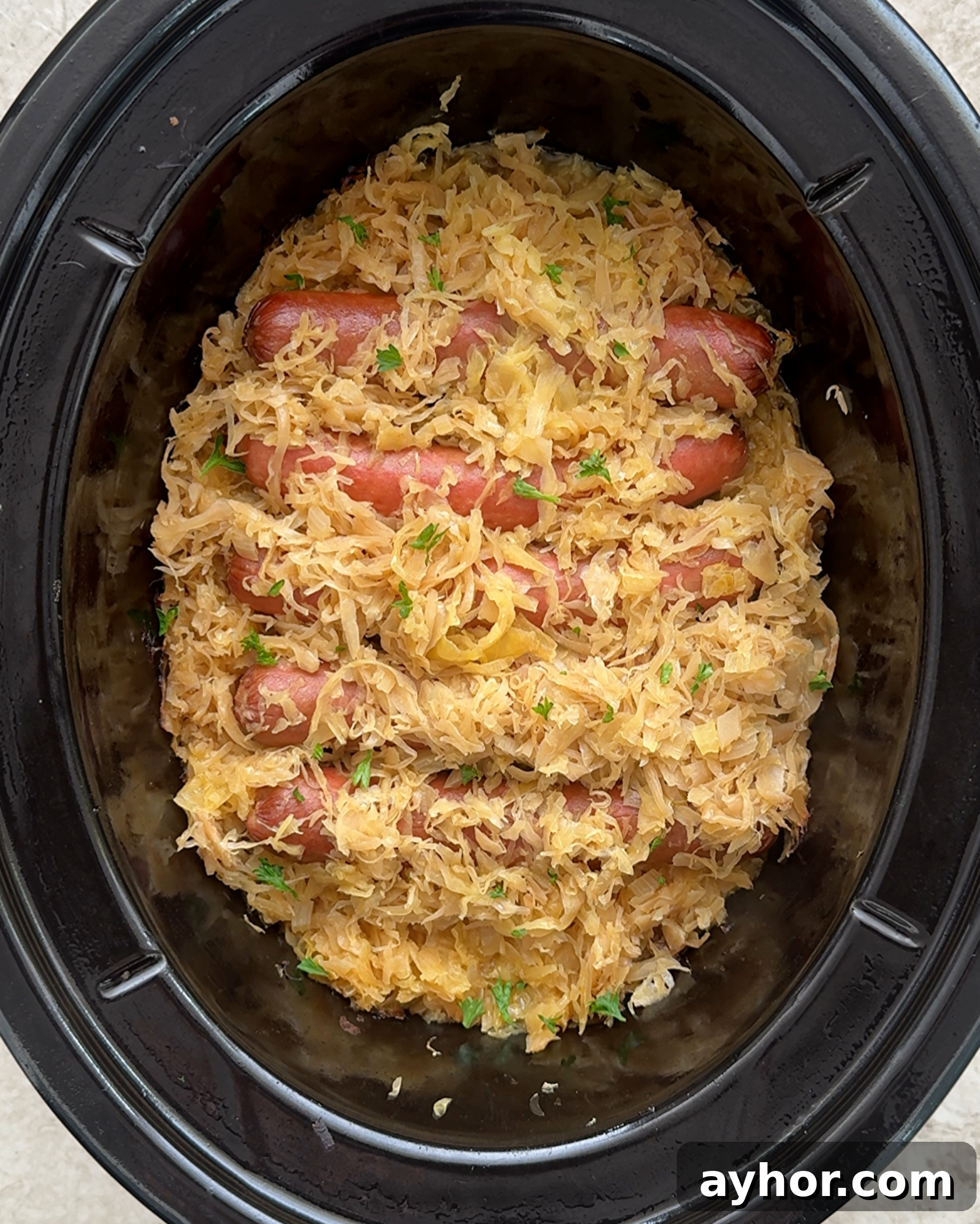 overhead shot of cooked hot dogs covered in sauerkraut a black slow cooker 