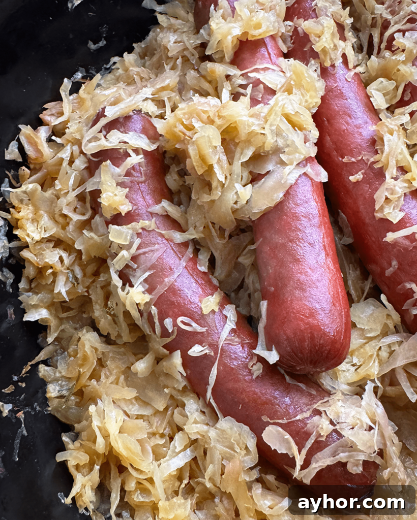close of shot of cooked hot dogs in a black slow cooker covered in sauerkraut