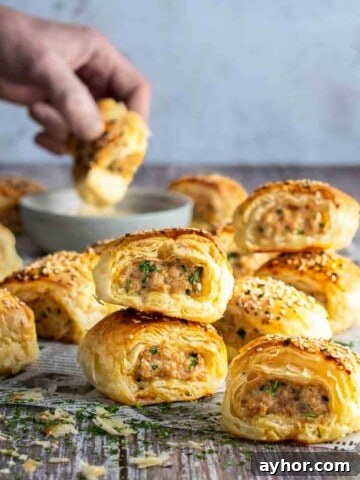 Chicken sausage rolls scattered on a table with a hand in the background dipping a sausage roll into sauce.