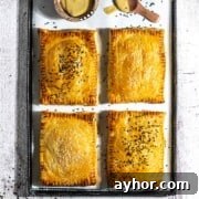 Four cheese and onion pasties on a baking sheet with a small bowl of mustard.