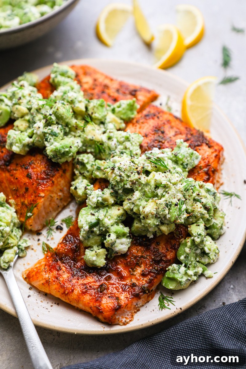 Baked Salmon with Creamy Avocado and Feta Crumble 8 A close up photo of baked salmon topped with avocado and feta surrounded by fresh dill and lemon wedges