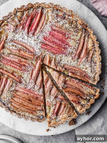 Rhubarb frangipane tart on a round marble platter with two slices cut.