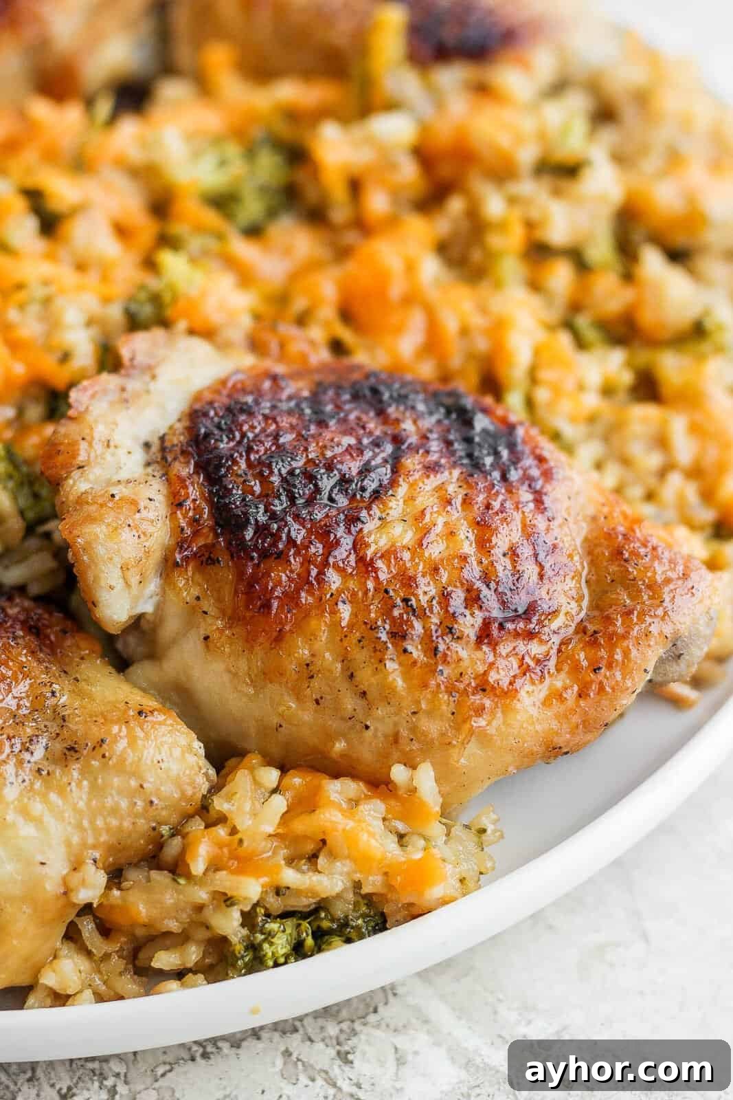 A seared chicken thigh on a white plate with cheesy rice and broccoli.
