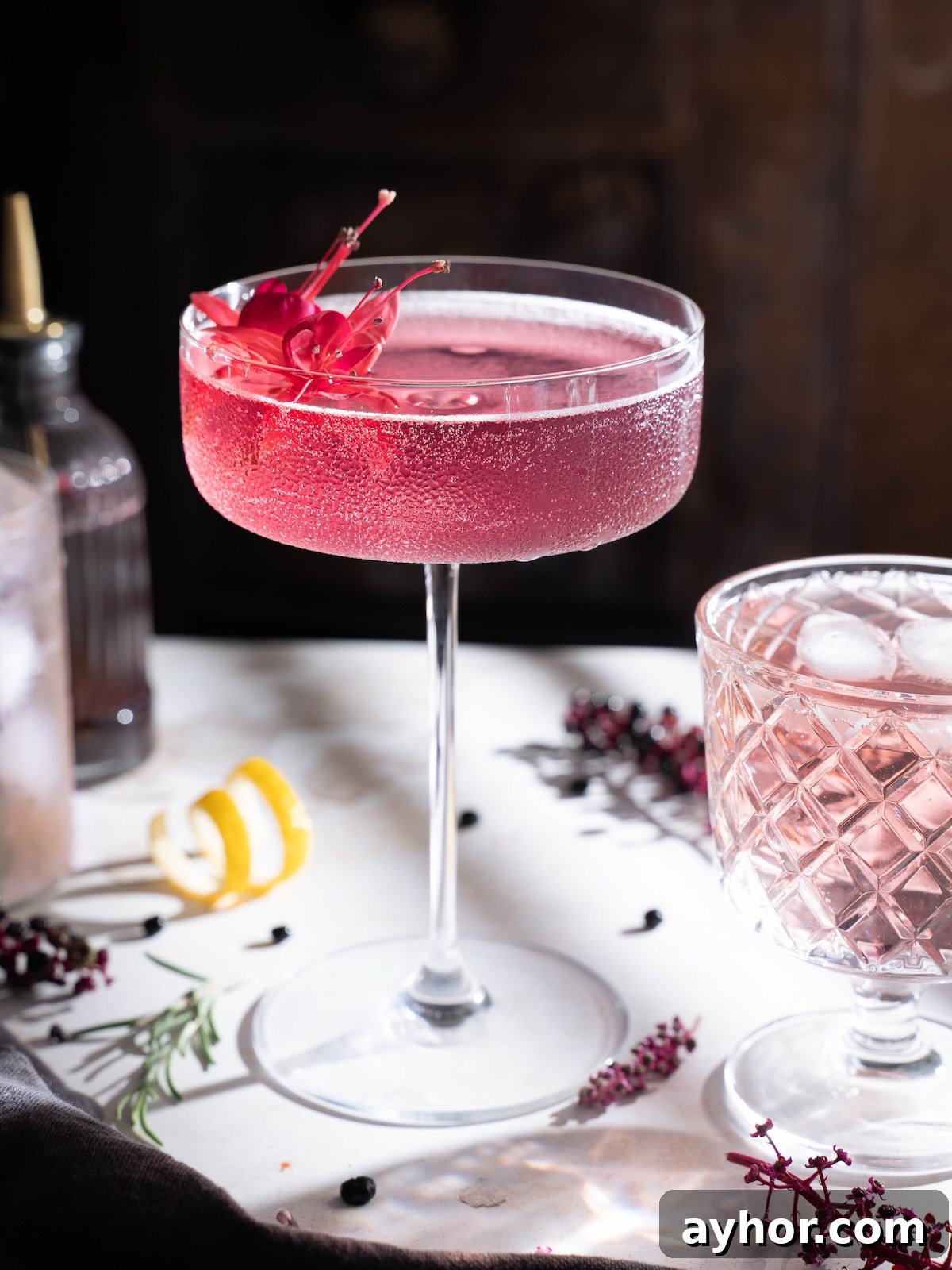 A beautifully pink elderberry cocktail served in a tall coupe glass with an edible flower garnish