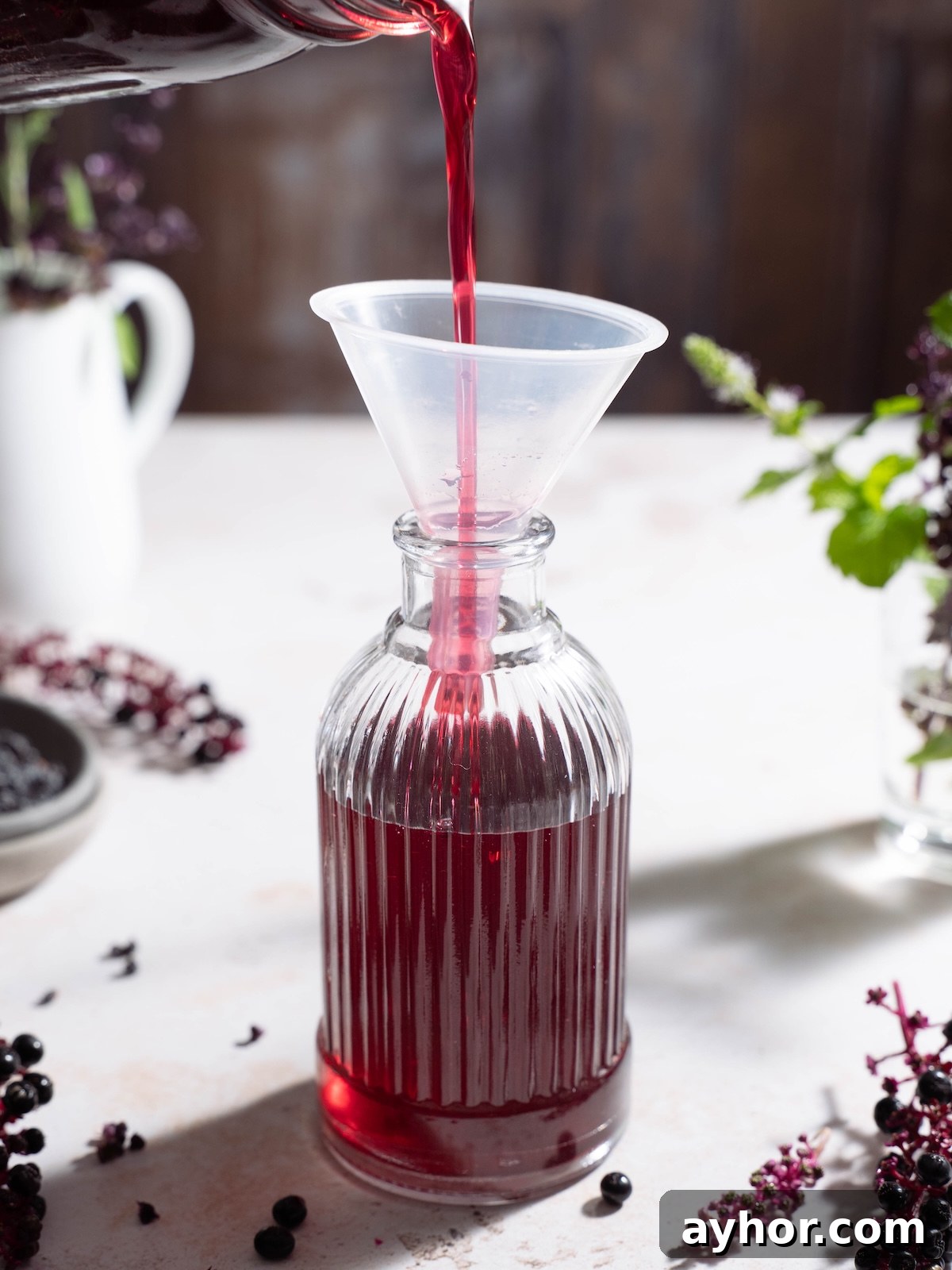 Pouring elderberry simple syrup into a glass jar