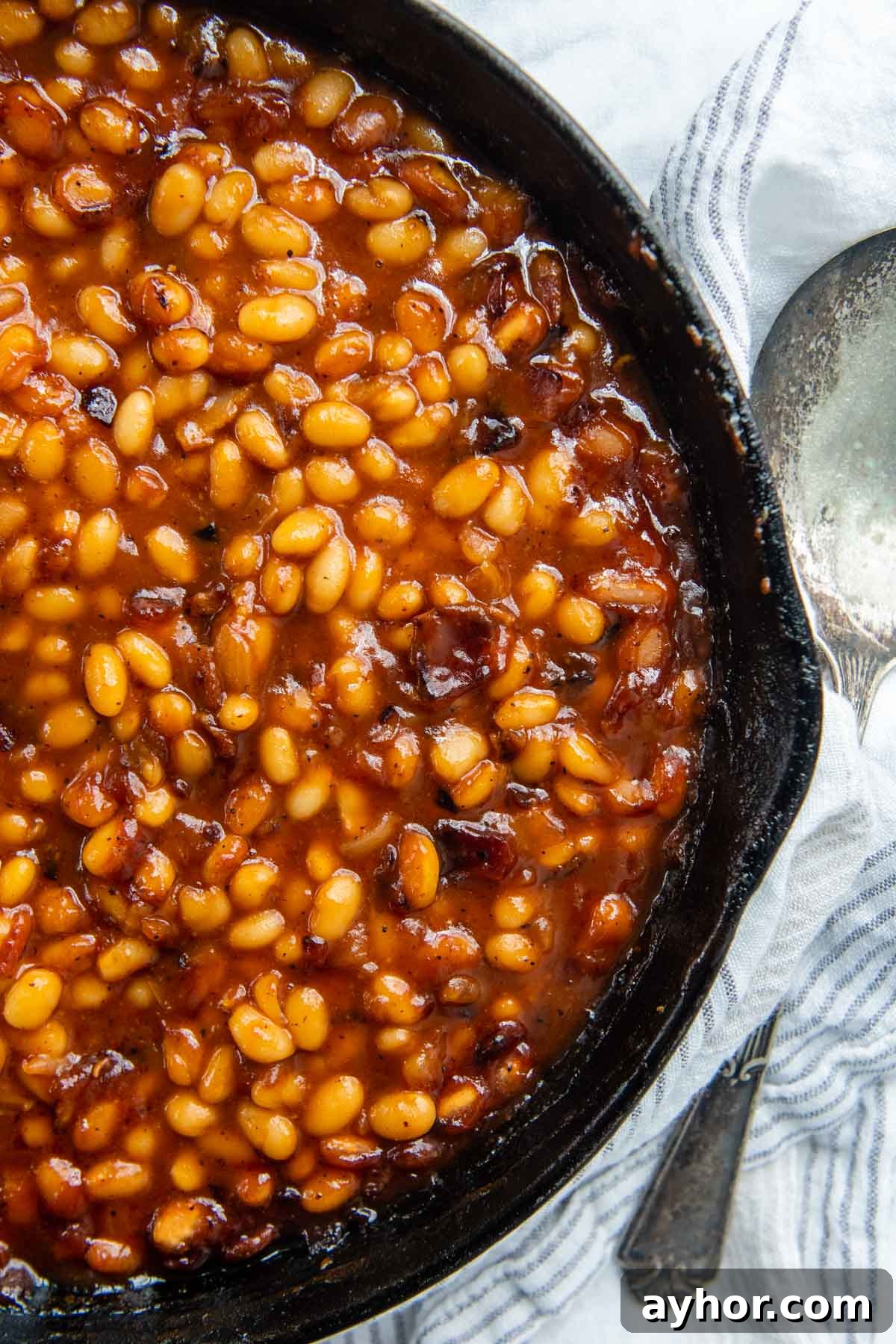 overhead shot of baked beans in a cast iron skillet with a spoon next to it.