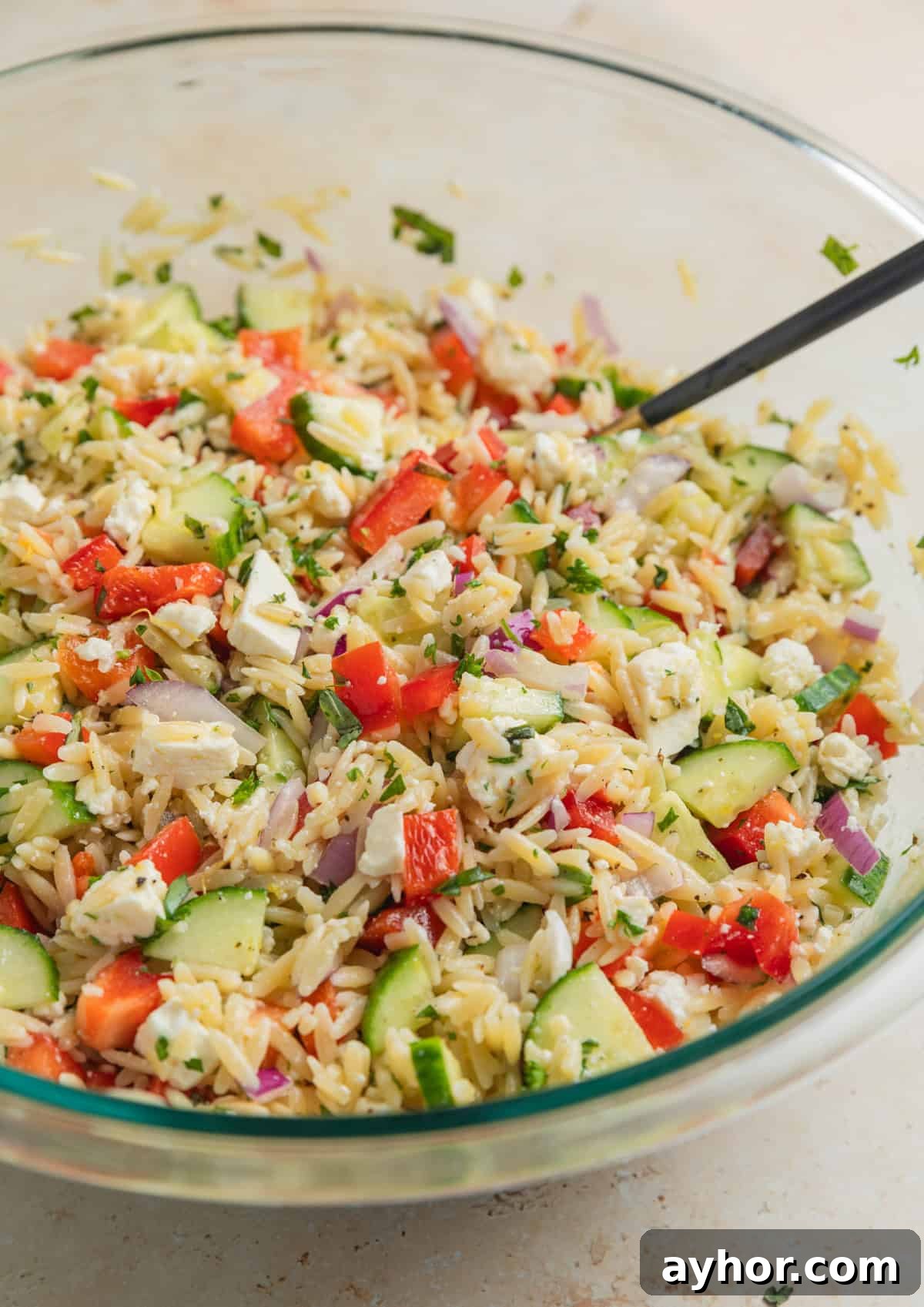 Prepared lemon orzo salad with spoon in glass mixing bowl.