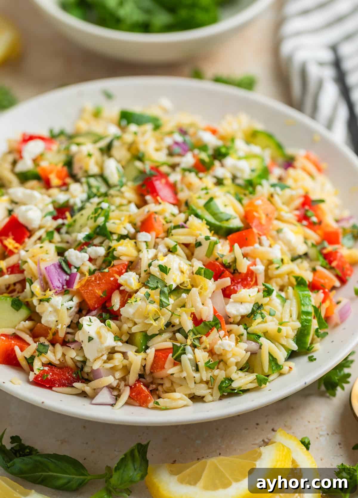 Orzo salad with feta, basil, parsley, cucumbers and more in white bowl.