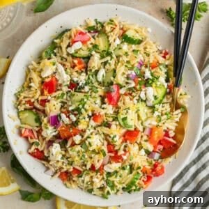 Lemon orzo salad with cucumber, bell pepper and feta in serving dish with serving utensils.