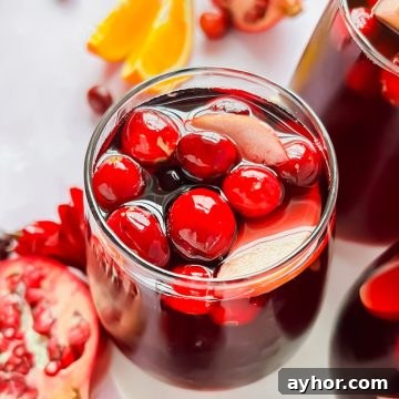 Festive Thanksgiving Sangria Recipe for Holiday Gatherings 13 glass full of thanksgiving sangria garnished with cranberries and apple slices.