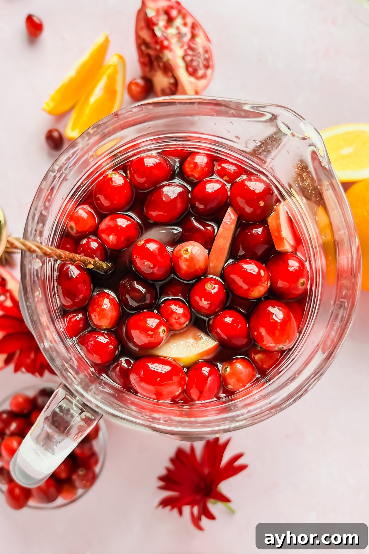 Festive Thanksgiving Sangria Recipe for Holiday Gatherings 7 pitcher full of thanksgiving sangria garnished with cranberries and apple slices surrounded by additional fruit.