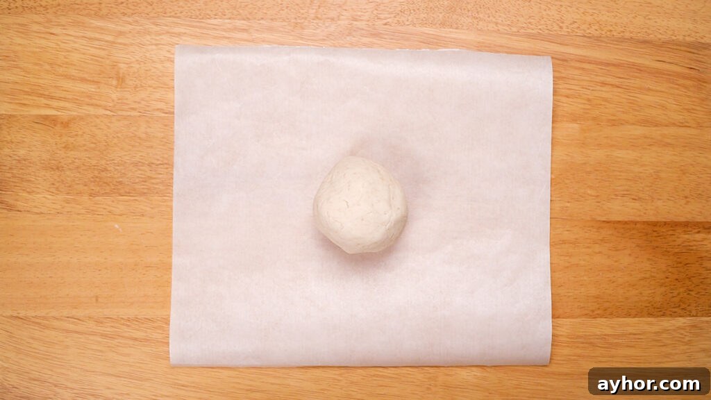 A ball of gluten-free cracker dough placed between two sheets of parchment paper on a wooden surface, prepared for rolling out.