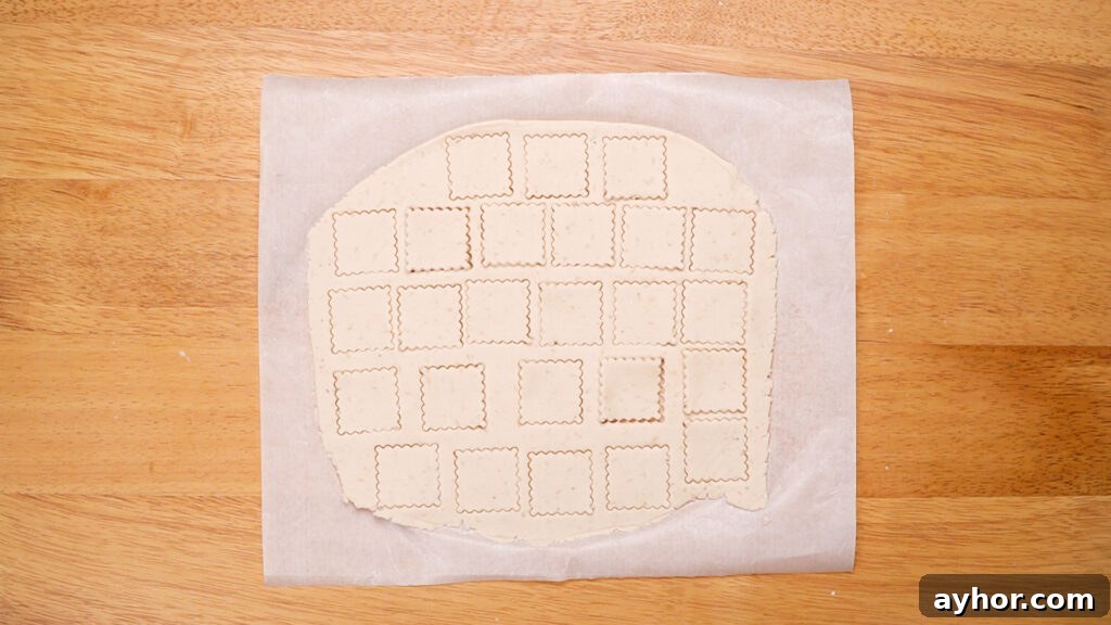 The rolled-out dough with neatly cut square cracker shapes, showing the uniformity of size and thickness for even baking.