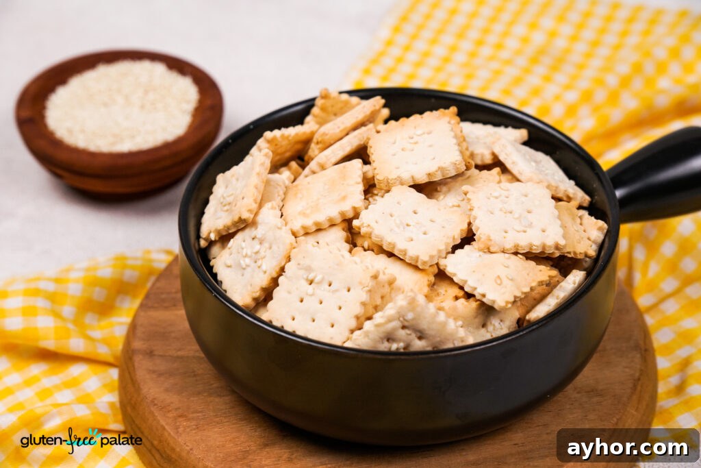 Crispy Homemade Gluten-Free Crackers 15 A black bowl filled with square, golden-brown gluten-free crackers topped with sesame seeds, placed on a wooden board with a yellow checkered cloth and a small wooden bowl of sesame seeds in the background.