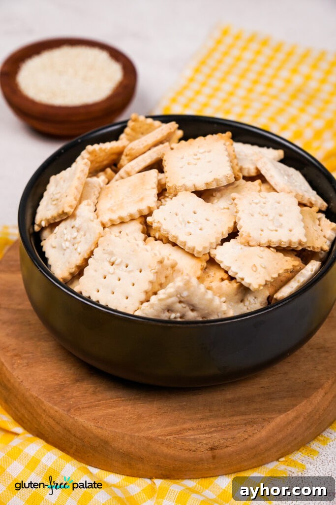 Crispy Homemade Gluten-Free Crackers 4 A top-down view of a bowl filled with crispy gluten-free crackers, with sesame seeds sprinkled on top and a yellow gingham cloth underneath.