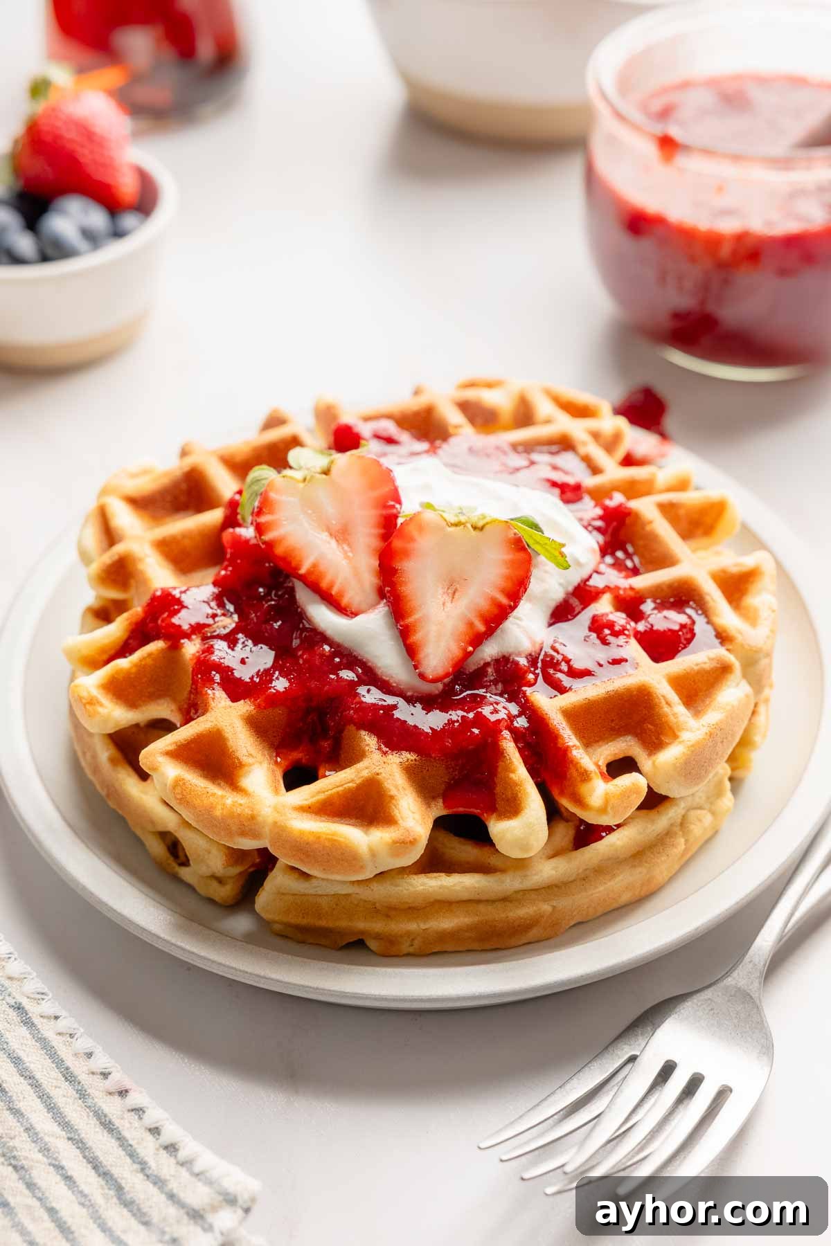 Two Belgian waffles topped with strawberry sauce, whipped cream and strawberry cut in half.