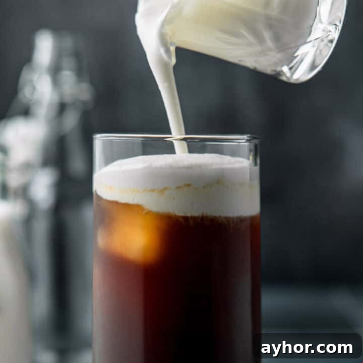 Pouring cold foam into a tall glass of iced coffee.