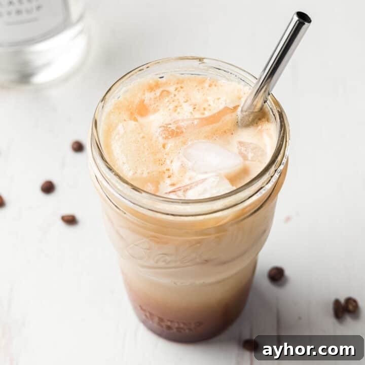 Frothy iced shaken espresso in a mason jar with ice and a stainless steel straw.